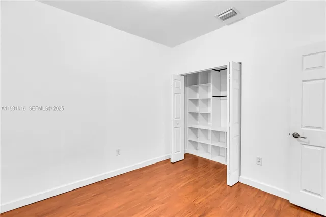 a view of an empty room with wooden floor and closet
