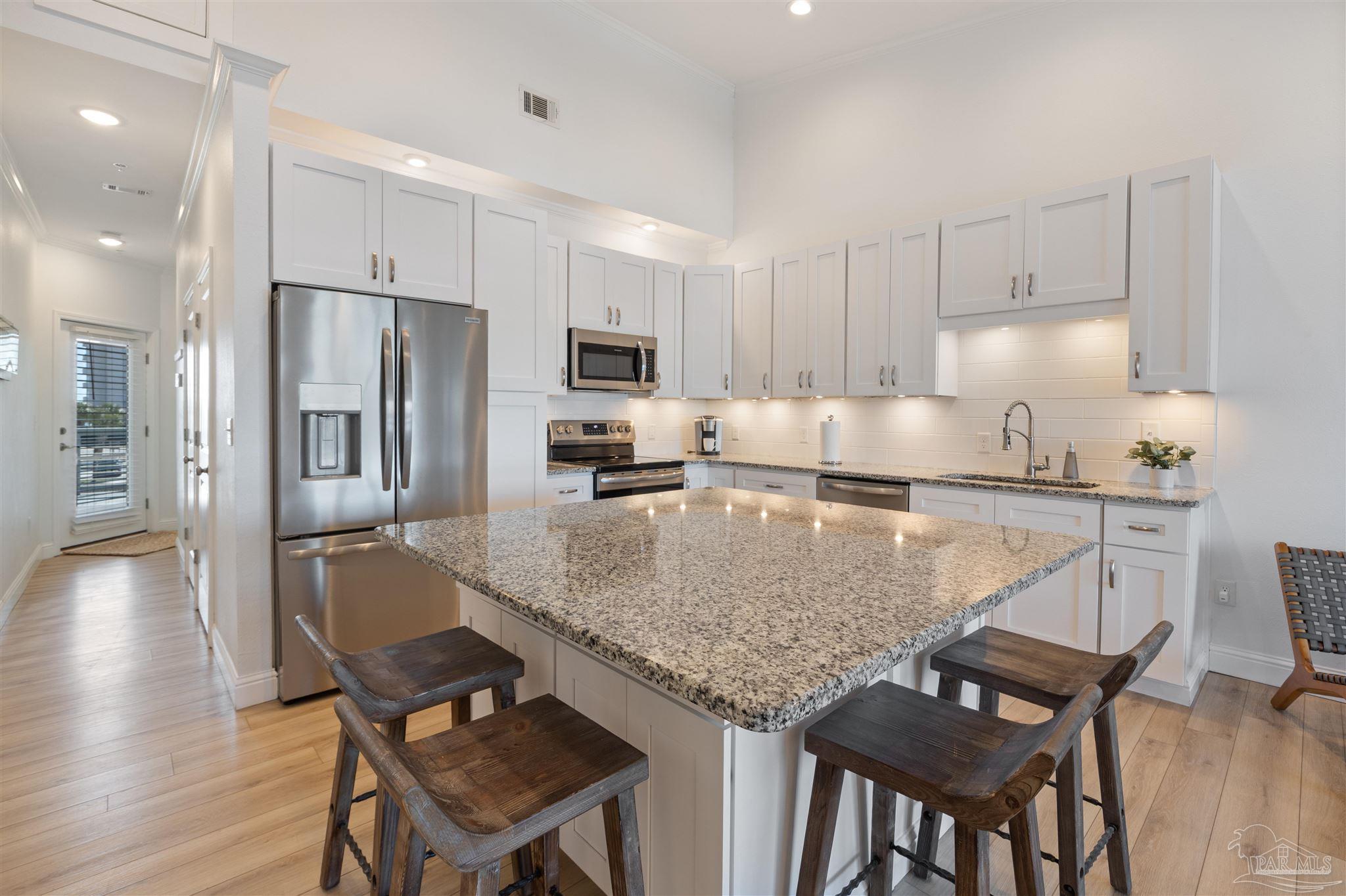 17290 Perdido Key Drive, Unit B2 Pensacola, FL 32507 - Photo 11 of 54 a kitchen with kitchen island granite countertop a table chairs microwave and refrigerator