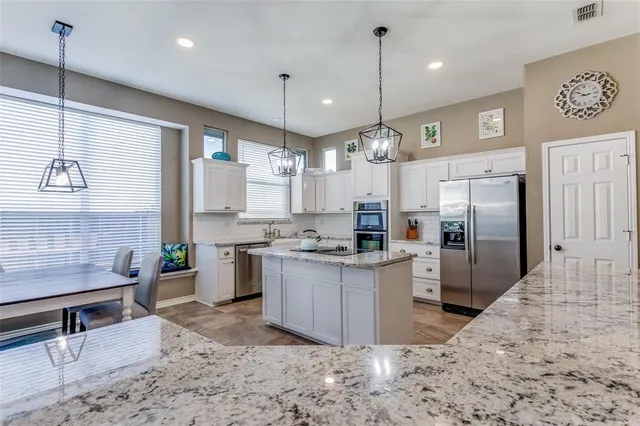 a kitchen with stainless steel appliances kitchen island granite countertop a refrigerator a stove a sink dishwasher a oven with white cabinets and wooden floor