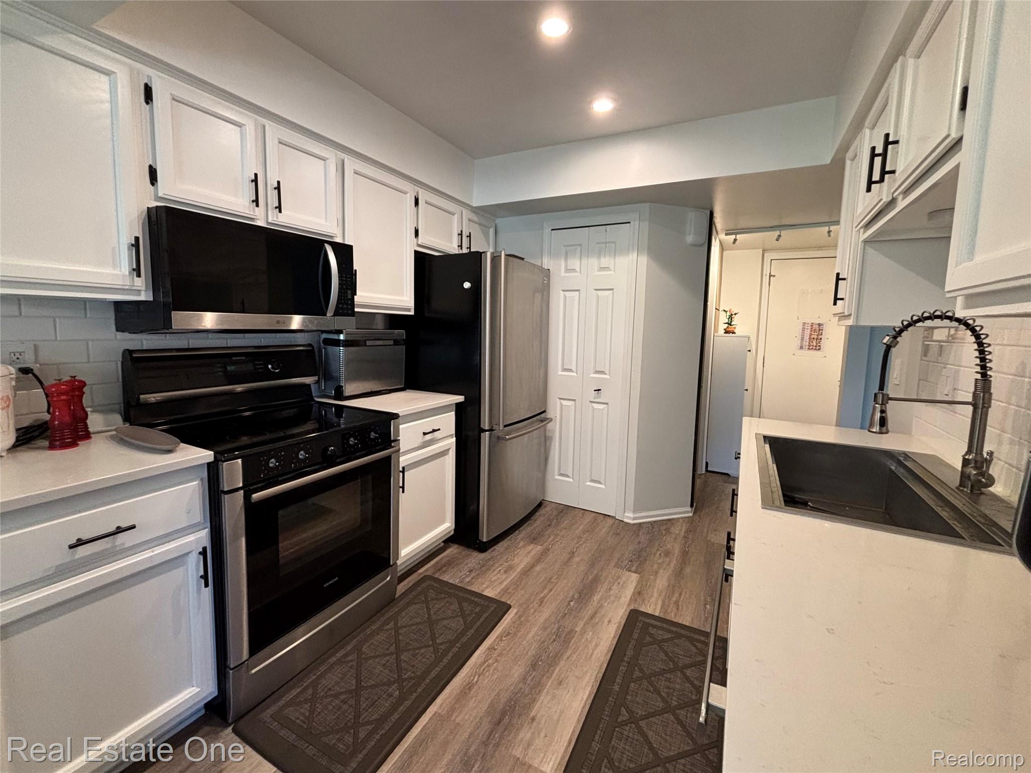 66 Meadow Wood Drive Rochester, MI 48307 - Photo 9 of 20 Contemporary kitchen featuring stainless steel appliances, white cabinetry with black hardware, light-toned countertops, subway tile backsplash, and wood-finish flooring
