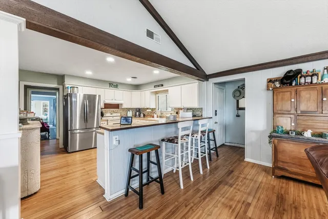 a kitchen with stainless steel appliances kitchen island granite countertop a refrigerator a stove a sink dishwasher and white cabinets with wooden floor
