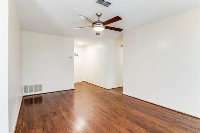 an empty room with wooden floor ceiling fan and windows