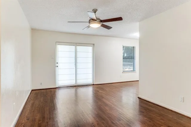 an empty room with wooden floor ceiling fan and windows