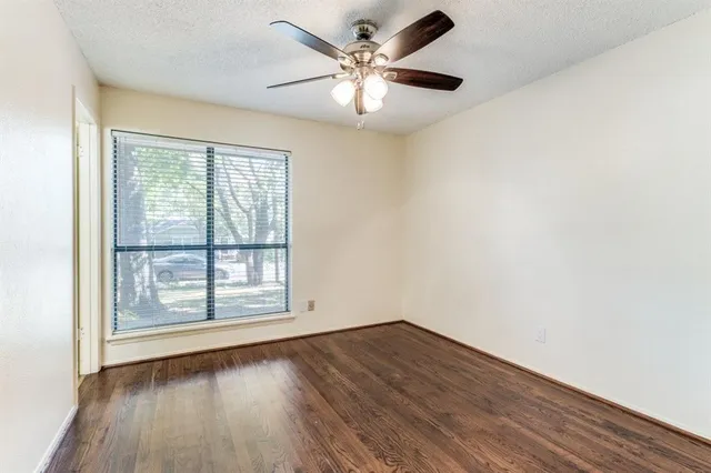 an empty room with wooden floor chandelier fan and windows