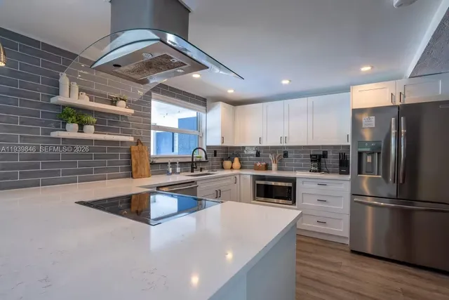 a kitchen with granite countertop a refrigerator a sink dishwasher a stove and white cabinets with wooden floor