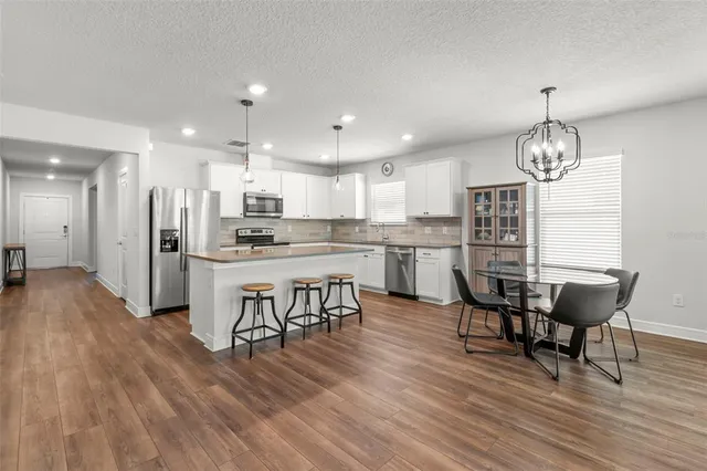 a view of a dining room and livingroom with furniture wooden floor a rug a flat screen tv a painting and a chandelier