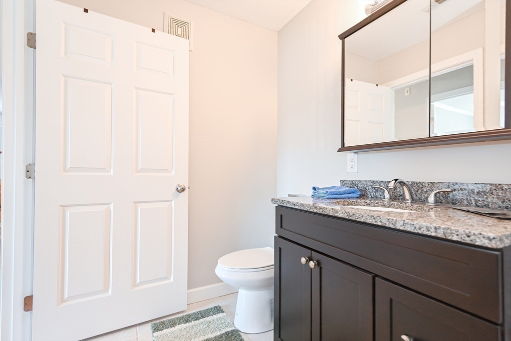 84 Mill Street, Unit 304 Woonsocket, RI 02895 - Photo 22 of 25 a bathroom with a granite countertop sink a toilet and a mirror