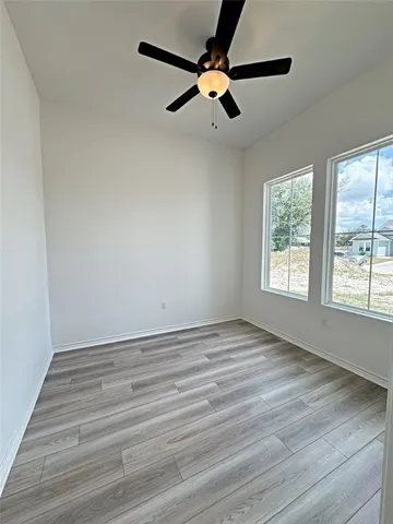 an empty room with wooden floor fan and windows