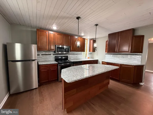 a kitchen with kitchen island granite countertop stainless steel appliances a stove refrigerator a sink a microwave oven and cabinets