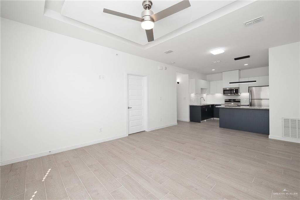 901 East Yuma Avenue, Unit 1901 McAllen, TX 78503 - Photo 4 of 9 Unfurnished living room with light wood-style flooring, a ceiling fan, and a raised ceiling