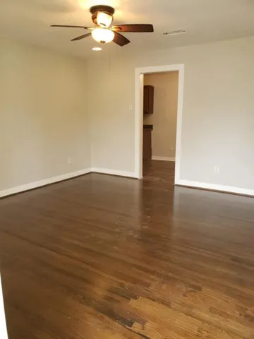 a view of an empty room with wooden floor and a ceiling fan