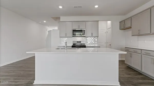 a kitchen with stainless steel appliances a sink a stove a microwave a refrigerator a cabinets and wooden floor