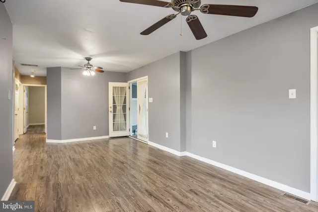 a view of an empty room with wooden floor and a ceiling fan