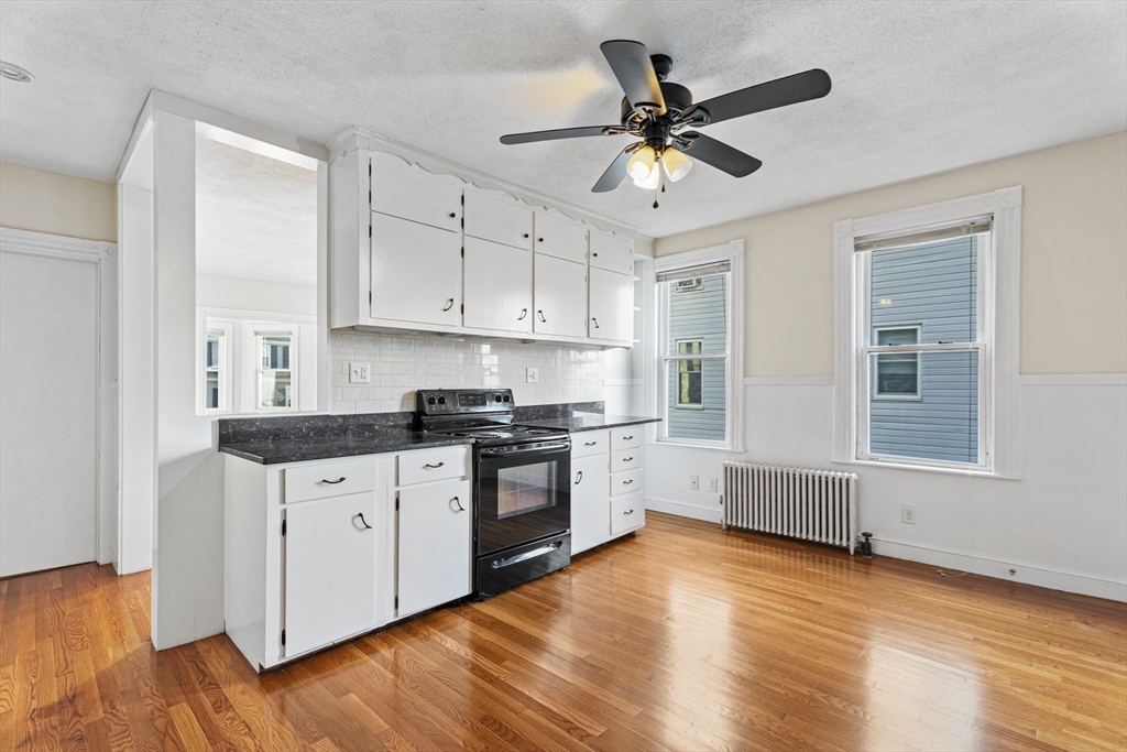 15 Sturgis Street Woburn, MA 01801 - Photo 6 of 38 a kitchen with granite countertop a stove a sink and white cabinets with wooden floor next to windows