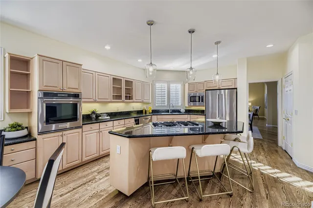 a kitchen with stainless steel appliances granite countertop a stove top oven a refrigerator a sink and chairs