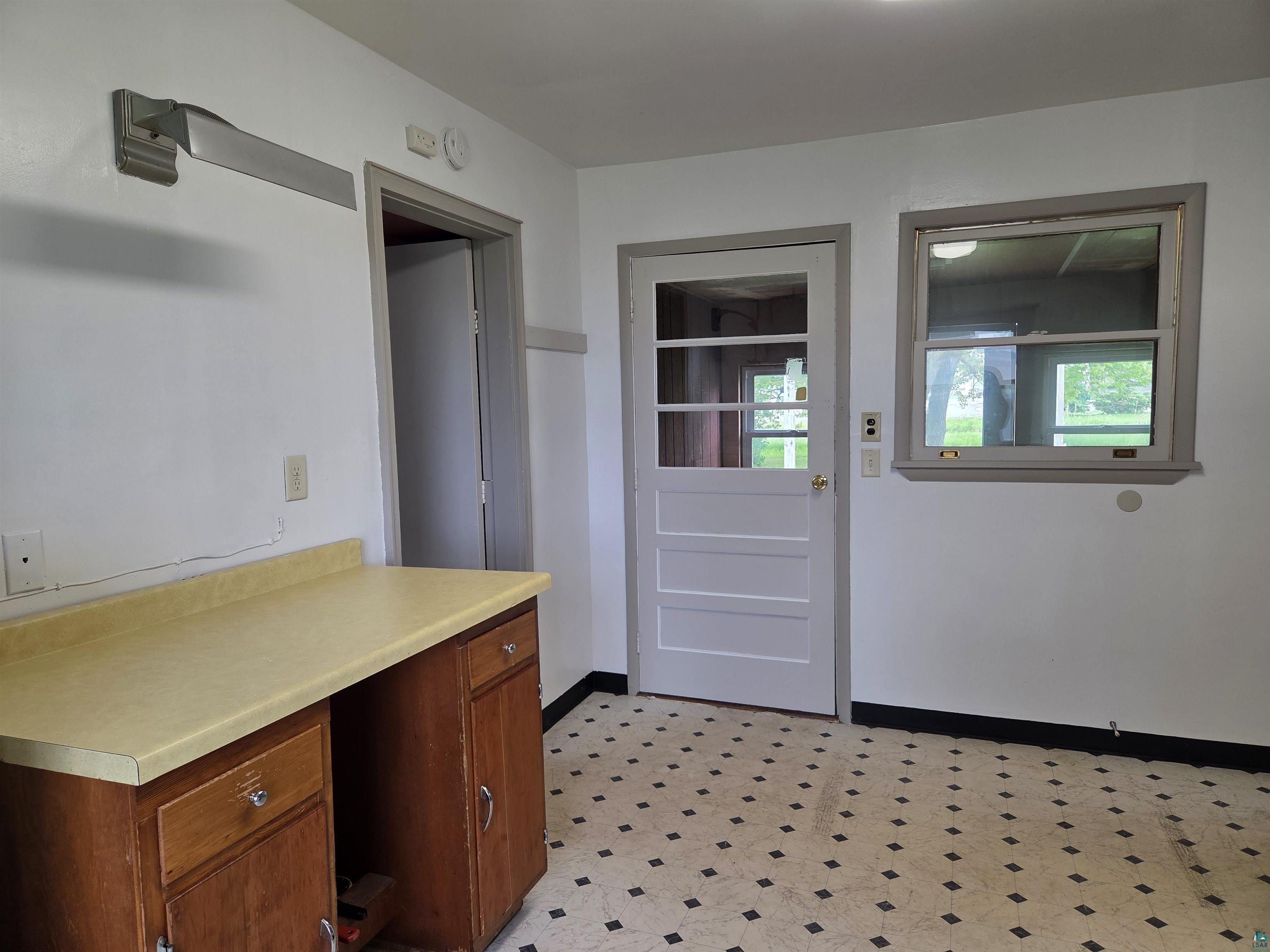 56 East 2nd Street Superior, WI 54880 - Photo 16 of 18 White paneled door with glass inserts, a single window, built-in wooden cabinetry with a light-colored countertop, and patterned floor tiles