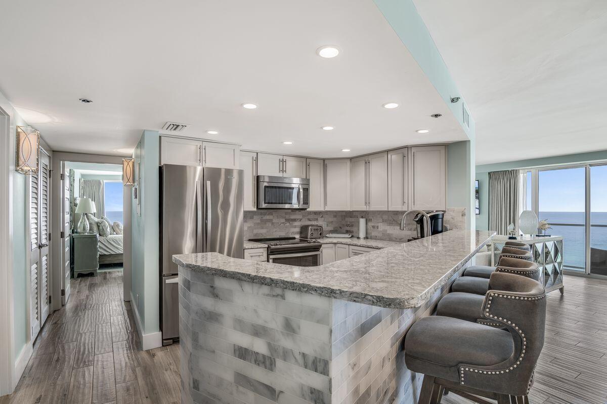 4323 Beachside 2, Unit 323 Miramar Beach, FL 32550 - Photo 15 of 41 a kitchen with stainless steel appliances granite countertop a refrigerator a stove a sink a dining table and chairs with wooden floor