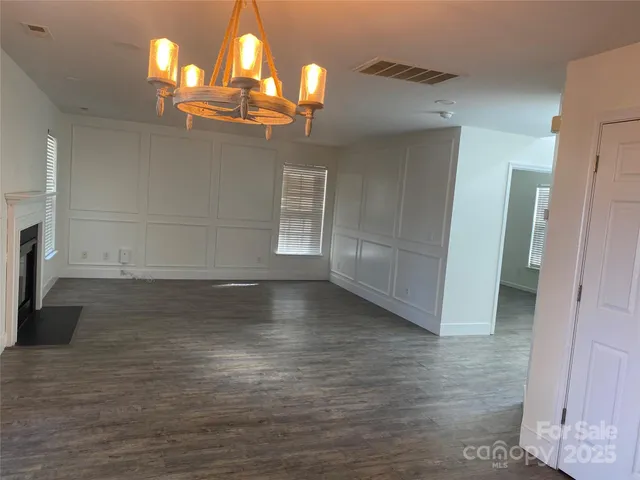 an empty room with wooden floor chandelier and windows