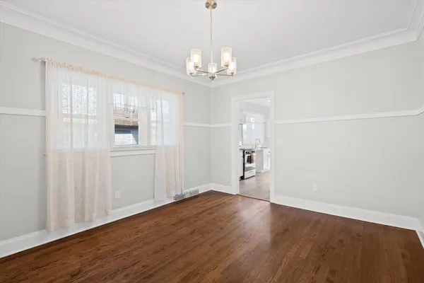 a view of an empty room with chandelier and wooden floor