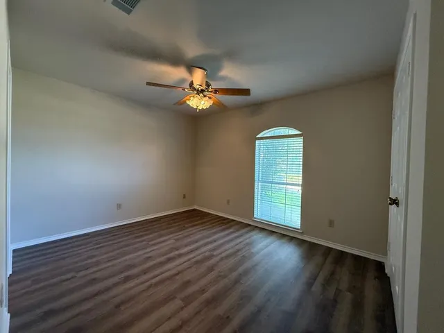 an empty room with wooden floor fan and windows