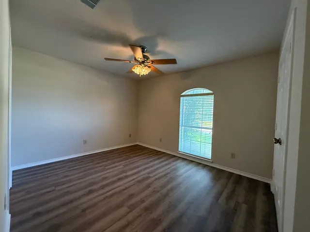 an empty room with wooden floor fan and windows