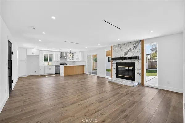 an empty room with wooden floor fire place and kitchen view