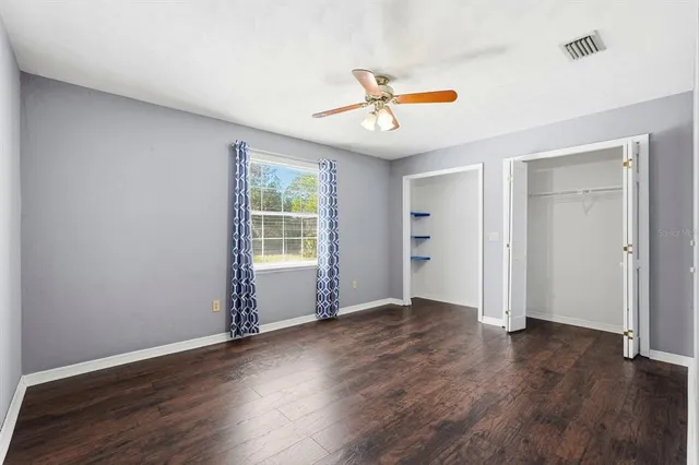 an empty room with wooden floor fan and windows