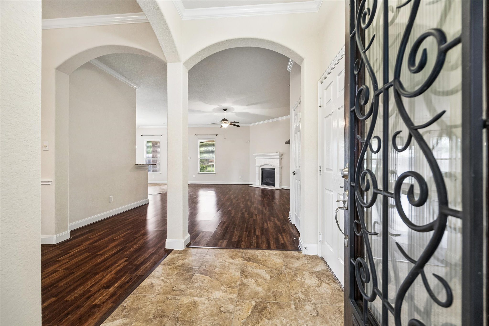 2214 Wembley Way Rosenberg, TX 77471 - Photo 7 of 35 Foyer with decorative wrought iron entry door, tile flooring, and arched doorways opening to a living area with wood-finish flooring, a ceiling fan, and a fireplace with a white mantel