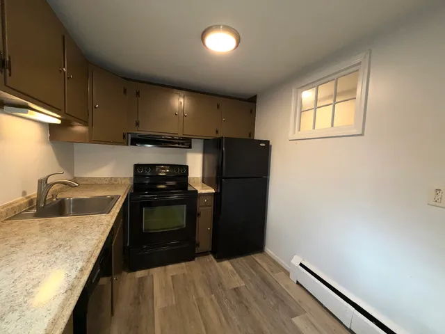 a kitchen with stainless steel appliances granite countertop a sink a stove a refrigerator cabinets and a wooden floor