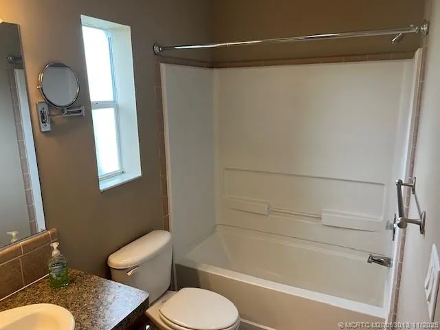 a bathroom with a granite countertop bathtub shower sink vanity and toilet