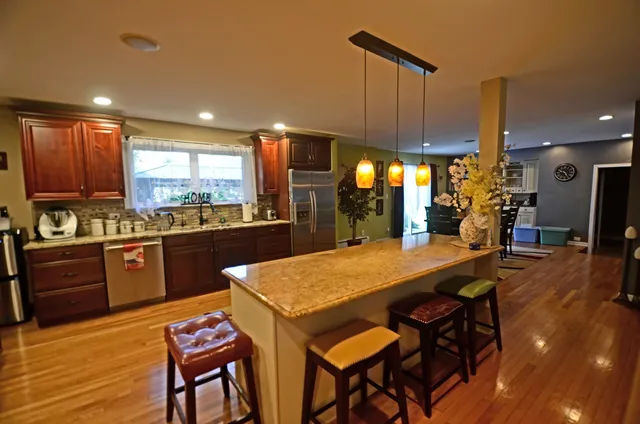 a kitchen with stainless steel appliances granite countertop a sink a stove a dining table and chairs with wooden floor