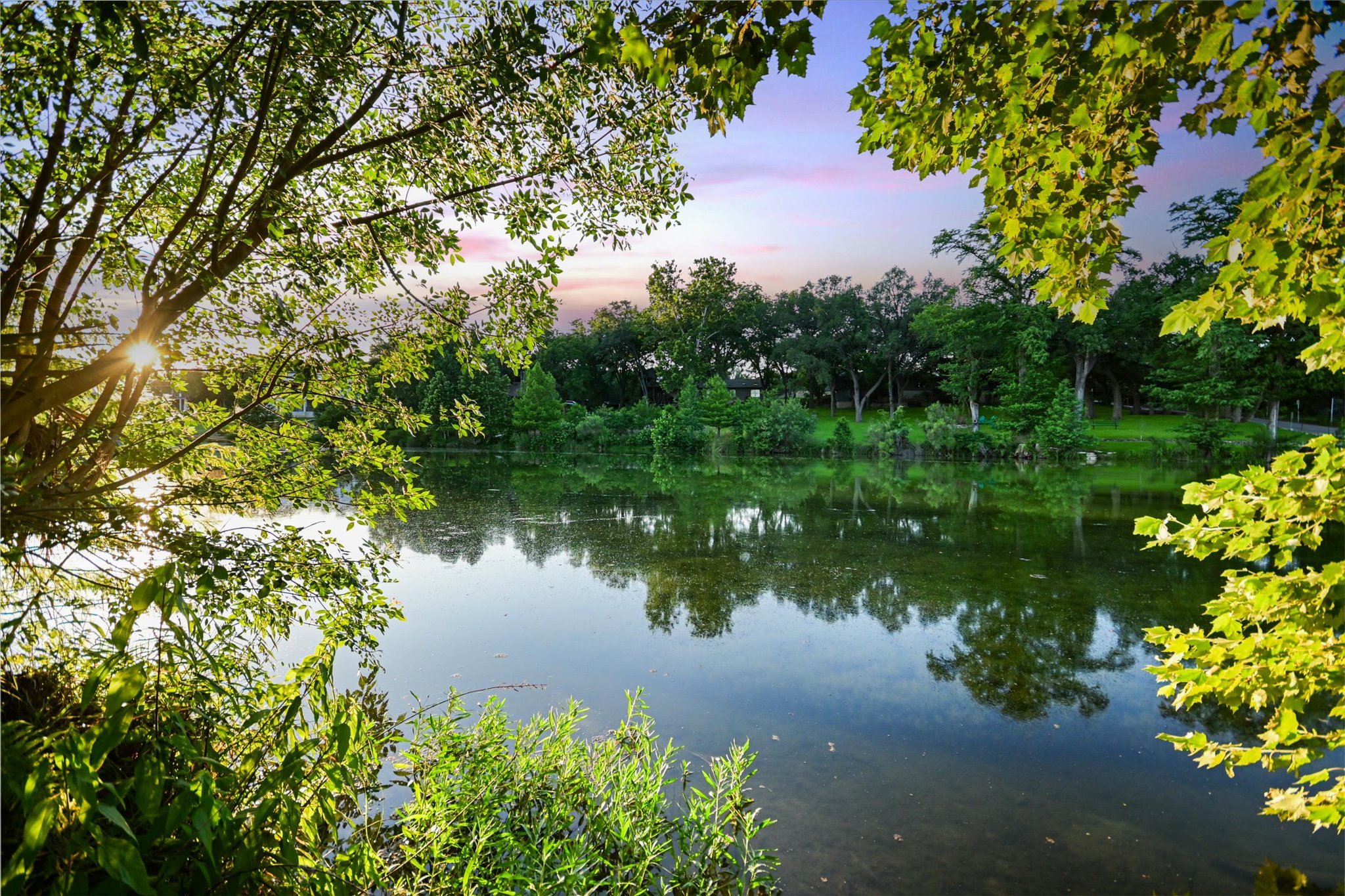 2411 Spoke Hollow Road Wimberley, TX 78676 - Photo 4 of 37 Lush foliage frames a serene lake, capturing a brilliant sunset's glow.