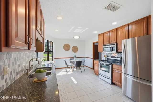 a kitchen with stainless steel appliances kitchen island granite countertop a refrigerator a stove and a sink with granite countertops