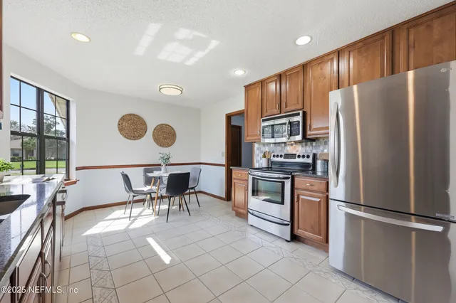 a kitchen with stainless steel appliances granite countertop a refrigerator a stove a sink and a dining table with white countertops