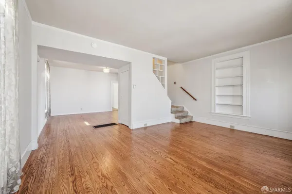 a view of an empty room with wooden floor and stairs