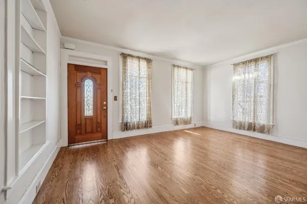a view of an empty room with wooden floor and a window