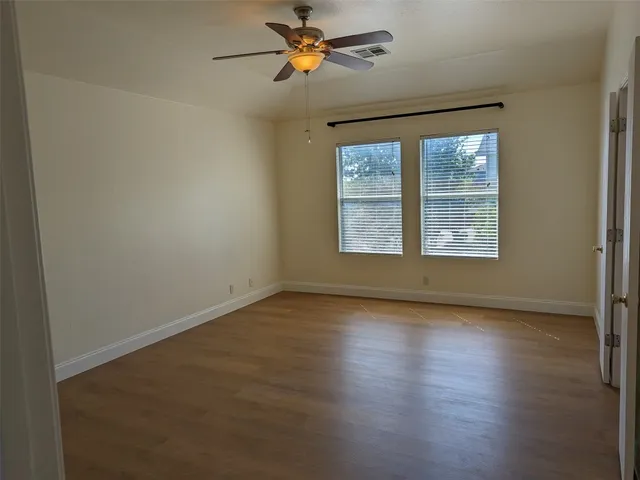 an empty room with wooden floor ceiling fan and windows