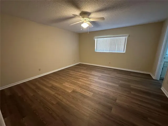 a view of an empty room with wooden floor and a ceiling fan