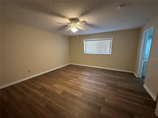 a view of an empty room with wooden floor and a fan