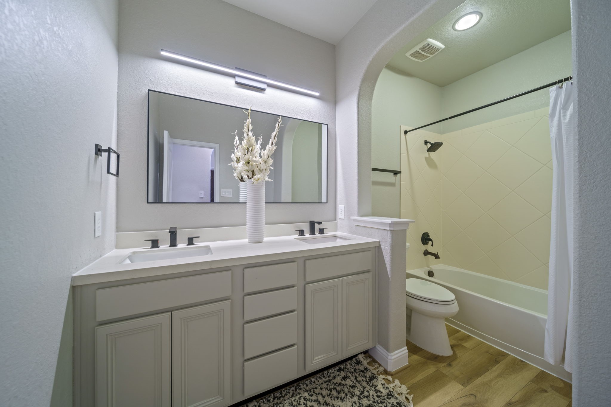 15 Inland Prairie Drive Tomball, TX 77375 - Photo 14 of 46 This bathroom has double sinks and serves as the bathroom for the front bedroom. It includes a tub-shower combo with a curved archway, complemented by neutral tones and wood-style flooring.