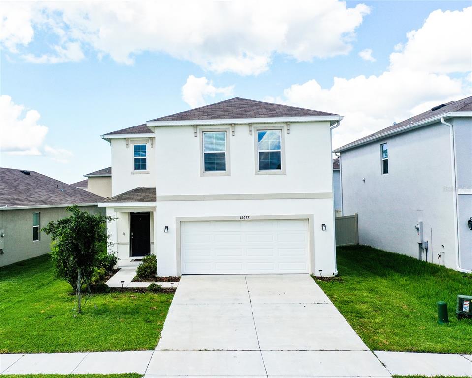a view of a white house with a yard plants and a large tree