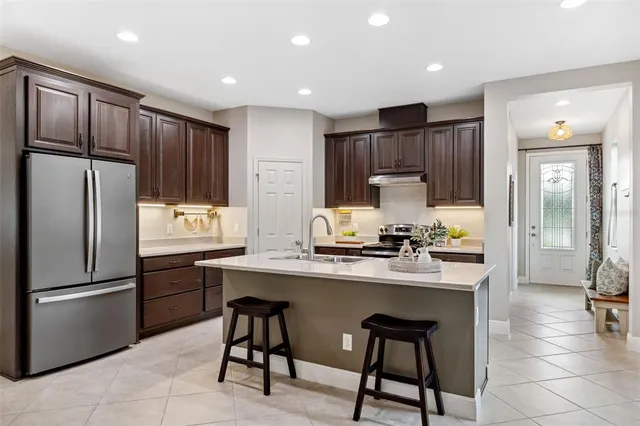 a kitchen with stainless steel appliances granite countertop a refrigerator a sink dishwasher a stove top oven a dining table and chairs with wooden floor