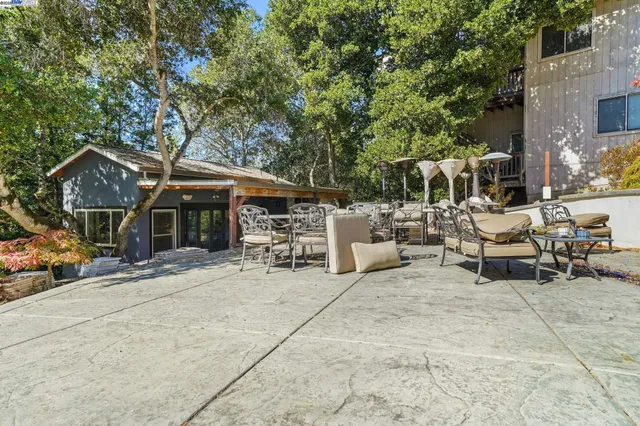 a view of a patio with table and chairs under an umbrella with large trees