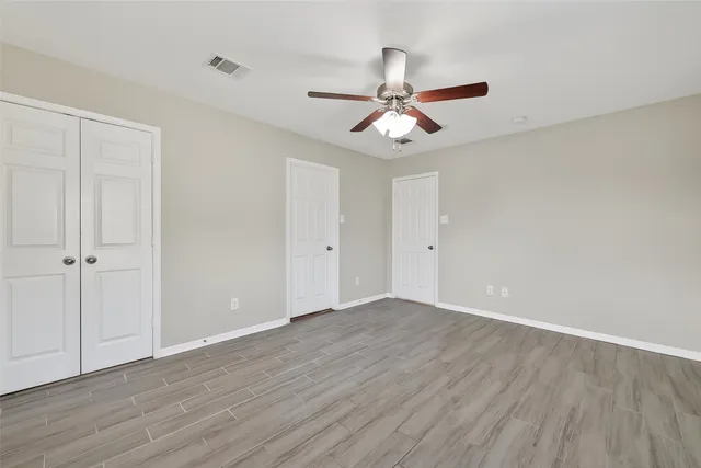 an empty room with wooden floor closet and fan