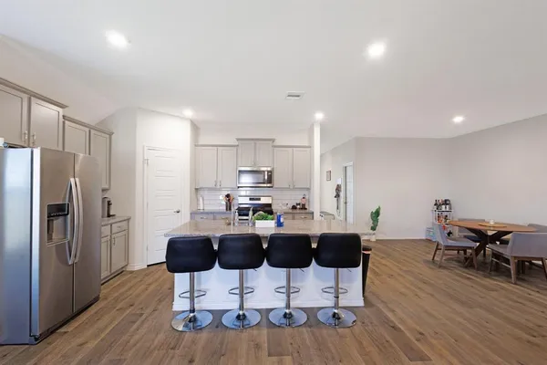 a kitchen with stainless steel appliances kitchen island granite countertop a dining table chairs refrigerator and sink