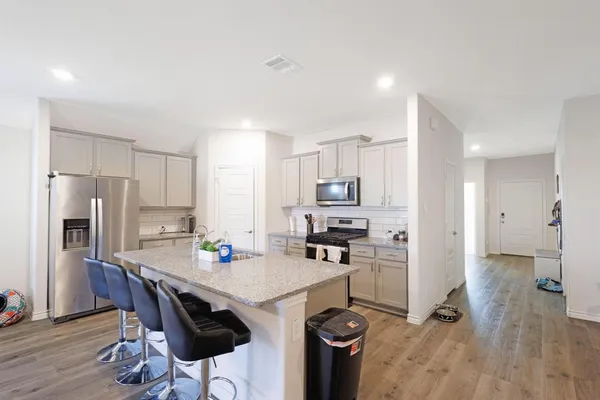 a kitchen with stainless steel appliances a stove a refrigerator a sink a dining table and chairs