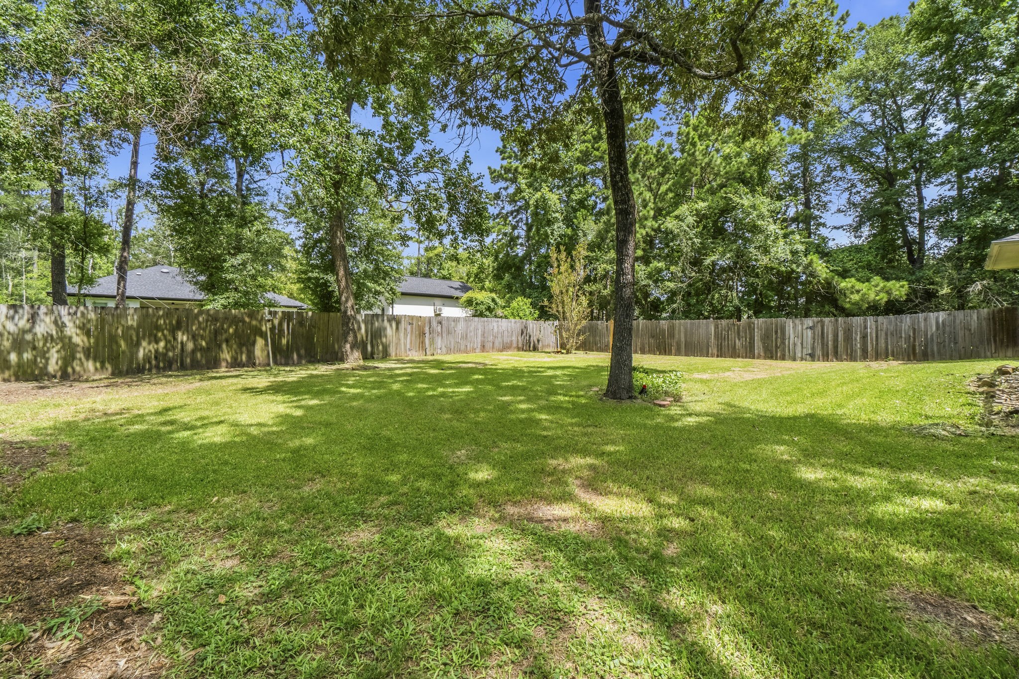 34019 Conroe Huffsmith Road Magnolia, TX 77354 - Photo 18 of 19 Spacious backyard with lush green grass, mature trees, and a wooden fence for privacy, offering a serene outdoor retreat.