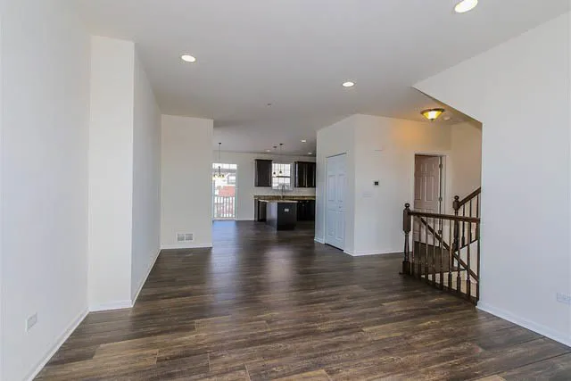 a view of an empty room with wooden floor and a kitchen