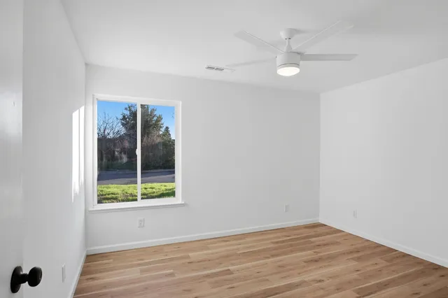 a view of an empty room with wooden floor and a window