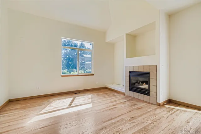 a view of an empty room with wooden floor a fireplace and a window